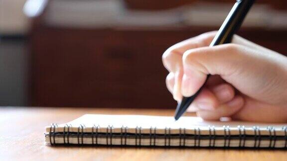 一个女人的手写在木桌上的空白笔记本上