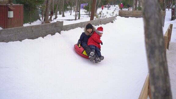 一个年轻的女人和她的小儿子有乐趣在油管在一个山区度假活动公园寒假