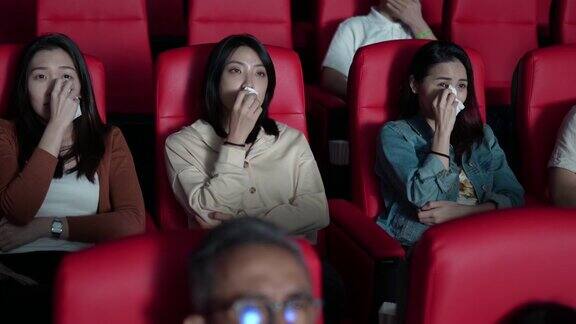 亚洲的中国女性朋友在电影院看感伤的电影在电影院用纸巾擦眼泪