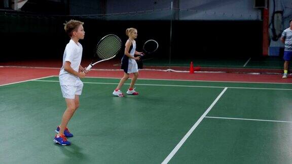 一队男孩和女孩在室内球场打网球年轻球员练习