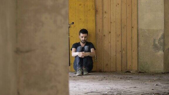 沮丧孤独一个年轻的悲伤的人靠在墙上向下看