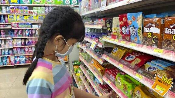 亚洲女孩戴着面具在杂货店寻找零食