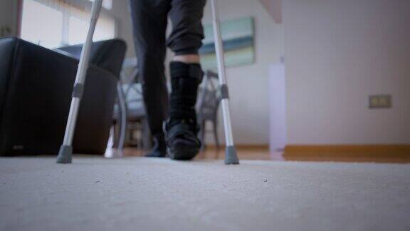 一个穿着黑色骨折靴的断腿男子试图在客厅里拄着拐杖走路