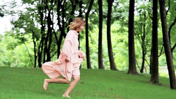 美丽的中国女人穿着粉红色的衣服在森林里奔跑夏天在自然概念休闲快乐的女孩赤脚在草地上奔跑侧视超慢的动作