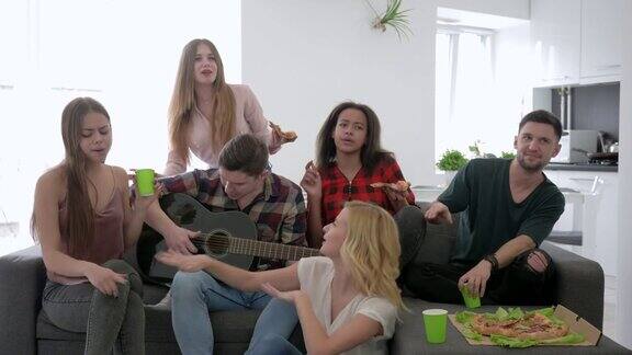 无忧无虑的一群朋友在家里聚会年轻人坐在沙发上玩吉他唱歌