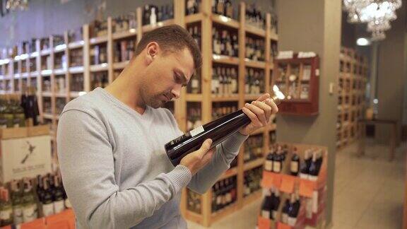 在一家葡萄酒商店里一个有吸引力的男人仔细地检查酒瓶标签上的成分酒店里的木架上放着酒瓶
