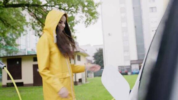 在雨中跳舞的年轻女子一个欢快的年轻女子在正在充电的电动汽车旁的雨中跳舞