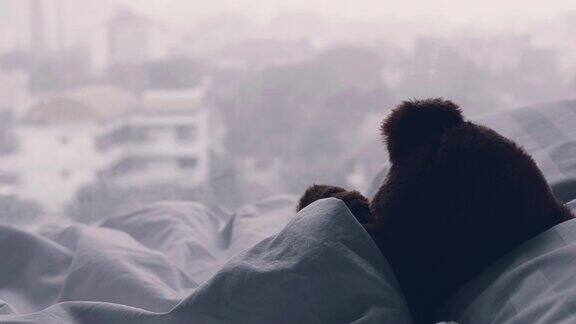 泰迪熊独自睡在床上白色的枕头和毯子对着窗户还有雨滴