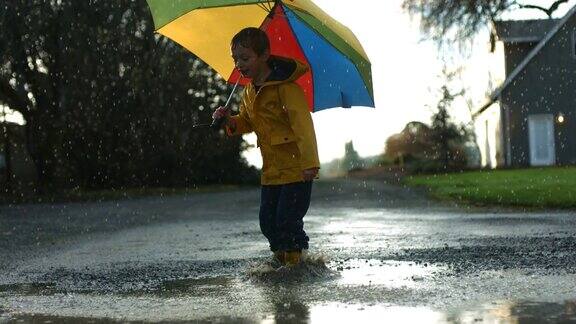小男孩拿着伞在水坑里跳慢镜头