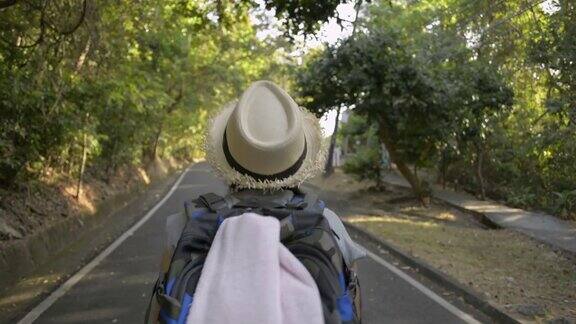 后视图亚洲女性徒步旅行者与背包穿过热带雨林戴着草帽的妇女走在小路上