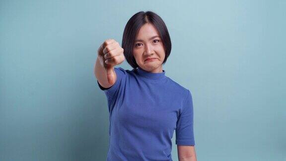 愤怒的亚洲妇女看着相机显示拇指向上向下站在孤立的蓝色背景4k的视频