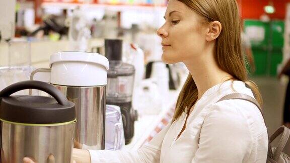 年轻女子在商店购买厨房电器拿起热水瓶选好水壶