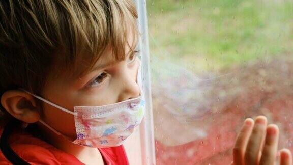 一个戴着医用口罩从窗户往外看的小男孩