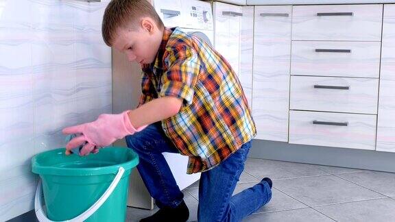 戴着橡胶手套的男孩把布压在桶上然后擦洗厨房的地板