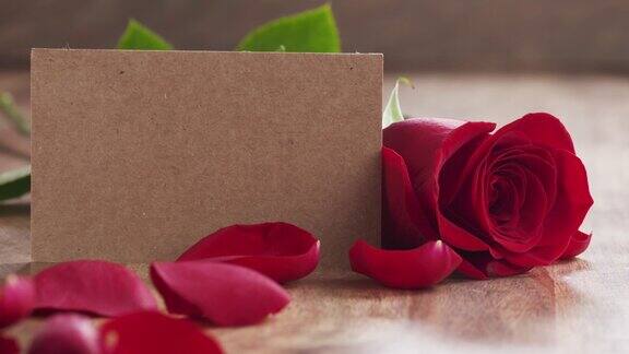 旧木桌上的一朵红玫瑰空纸卡上的花瓣缓缓飘落