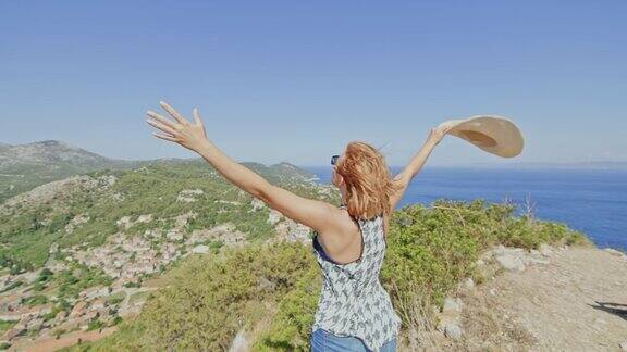 无忧无虑的女人伸开双臂站在风大、阳光灿烂的夏岛上眺望