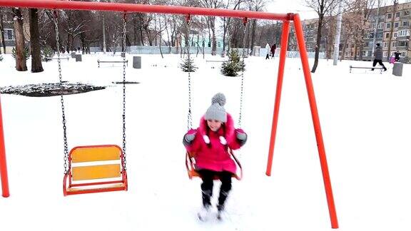 快乐的女孩在冬天霜冻的一天在公园里荡秋千