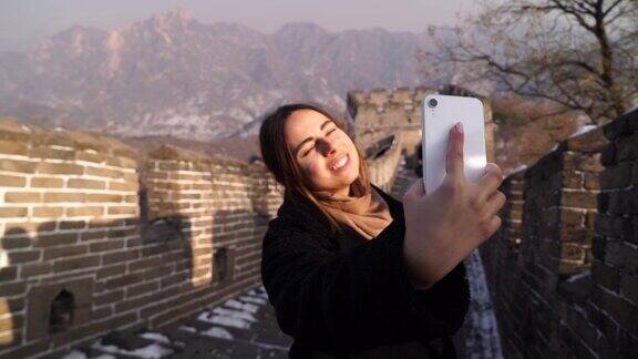 美丽的女人在亚洲旅行站在长城上自拍在日落的冬天快乐的年轻女子在长城上自拍