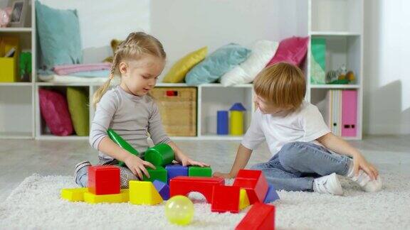 快乐的小男孩和小女孩在地板上玩玩具积木塔