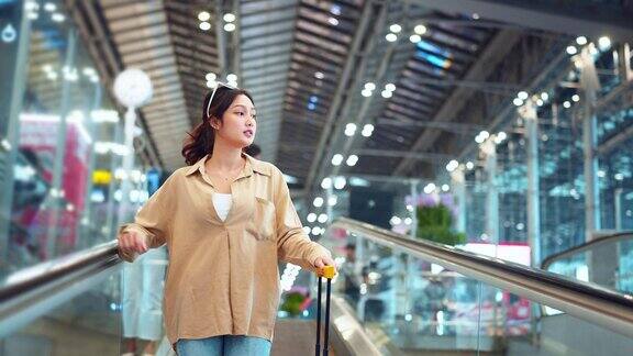 亚洲女游客带着简单的行李箱站在机场航站楼的移动人行道上旅游旅行