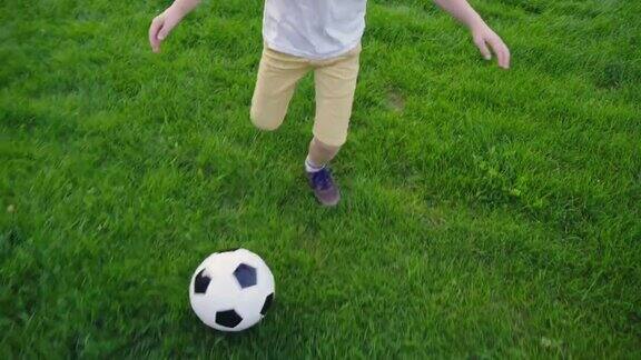 男孩在踢足球带着球的孩子跑过绿色的草地