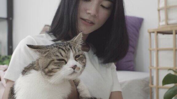 年轻的亚洲美丽的女人玩和抱着她的可爱的猫在卧室在家里的背景人与宠物之间的爱和友谊慢动作
