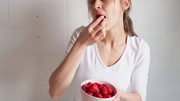 女人拿着一个盛着草莓的碗吃浆果
