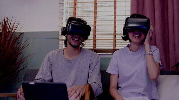 亚洲夫妇戴着现代虚拟现实眼镜坐在家里的客厅里看电影节日活动家庭娱乐技术幸福生活在一起metaverse概念
