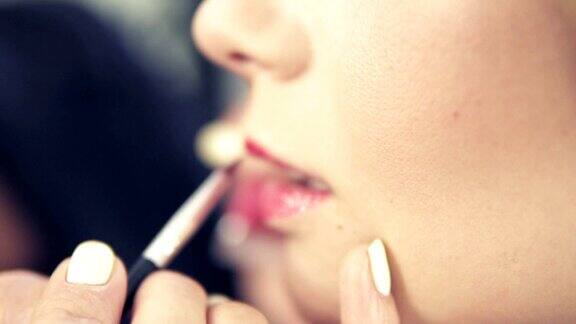 化妆师用口红刷画一个美丽女孩的嘴唇模型与口红嘴唇上涂着粉红色的口红流行色调的口红Slowmotion拍摄