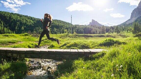 健康的女人在户外慢跑在小溪上的一座桥