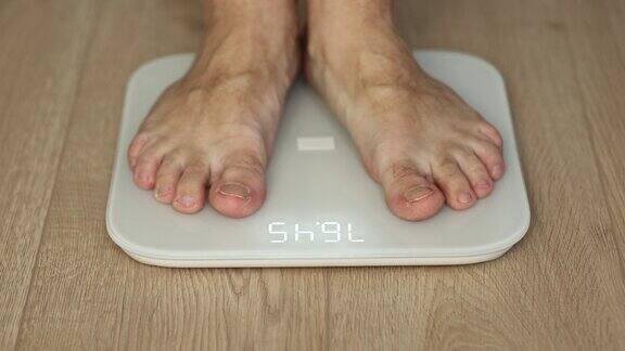 步行男性检查BMI体重下降人类赤脚测量身体脂肪超重男人的腿踩在浴室秤上减肥男子脚站立秤上的房间男人用体重秤测量体重