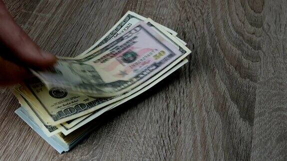 双手叠起许多美元叠在木桌上一张接一张的钞票