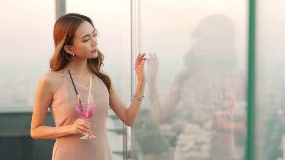 日落时分一名4K亚洲女子在摩天大楼的屋顶餐厅喝着鸡尾酒等朋友
