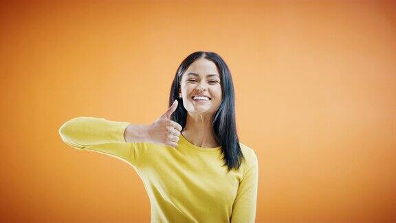 一段4k视频一名年轻女子对着橙色的录音室背景竖起大拇指