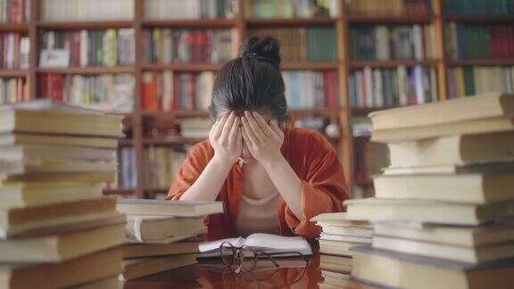 疲惫的亚洲学生在图书馆的书堆后面哭泣学业压力