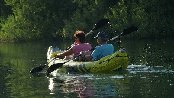 慢镜头特写:在夏日的夕阳下一对成熟的夫妇在美丽平静的河上划独木舟