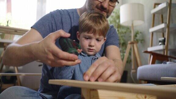 在好奇的蹒跚学步的儿子的帮助下父亲正在组装新家具