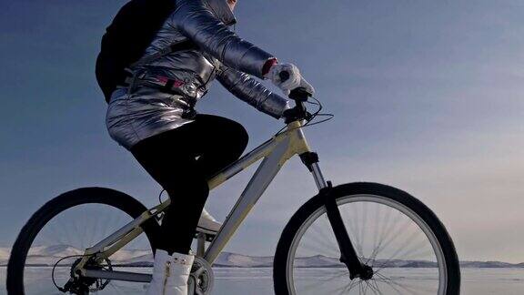 一个女人在冰上骑自行车这个女孩穿着银色的羽绒服背着自行车背包戴着头盔结冰的贝加尔湖的冰自行车的轮胎上覆盖着特殊的尖钉