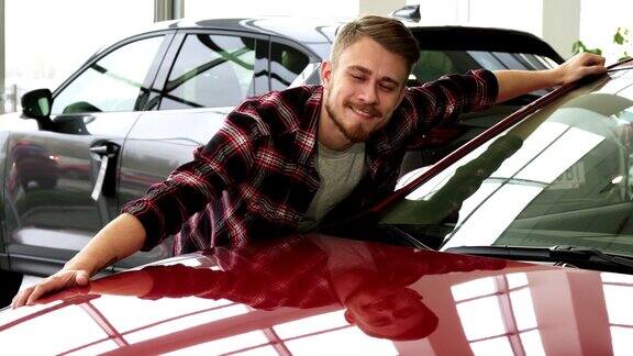 快乐的胡子英俊男子拥抱他的新汽车在经销商沙龙