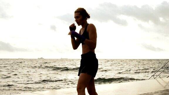 运动空手道女子使她的腿对着太阳的海边在慢动作侧踢美丽的女拳击手早上在沙滩上训练拳打脚踢