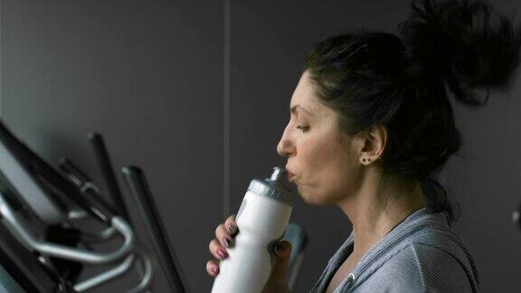 积极的女运动员在跑步机上喝水