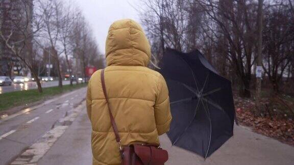 下雨天穿着黄色夹克撑着雨伞走路的女人