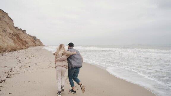 在秋天的海滩上一对家庭夫妇手牵手走在海边