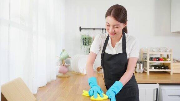 亚洲年轻清洁服务女工清洁厨房桌子在家里美丽的年轻女孩管家清洁工感到高兴并擦拭脏乱的烹饪柜台家务或杂务