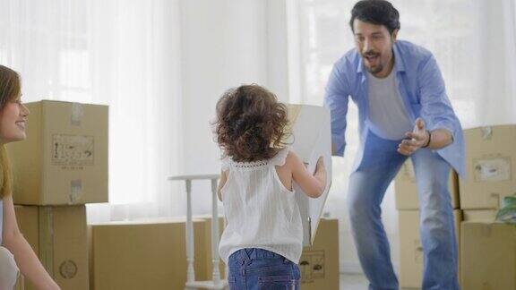 一对年轻的父母正在收拾纸箱准备搬入新家或公寓而他们可爱的小女儿则在客厅里帮忙拿起纸箱