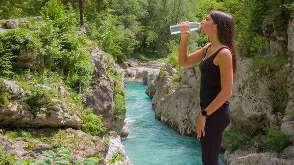快乐女游客在山间小溪边欣赏美景喝着水