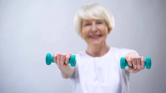 老女人拿着哑铃对着镜头微笑健康健康的生活方式