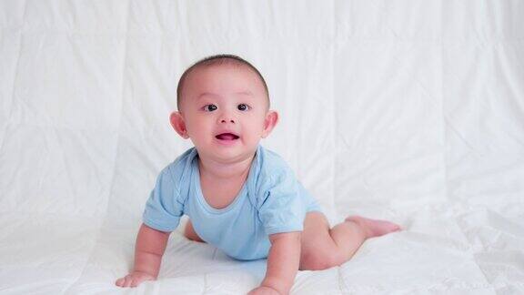 幸福的家庭可爱的亚洲新生宝宝穿着蓝色的衬衫躺在床上爬着玩着看着镜头笑着笑着开心的脸天真可爱的小婴儿为人父母和母亲节