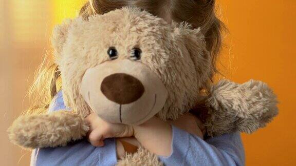 害羞的学龄前女孩躲在最喜欢的泰迪熊后面童年心理