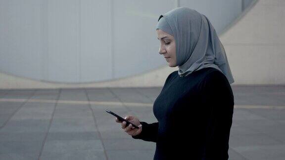 运动的穆斯林健身妇女戴着头巾使用智能手机(慢动作)